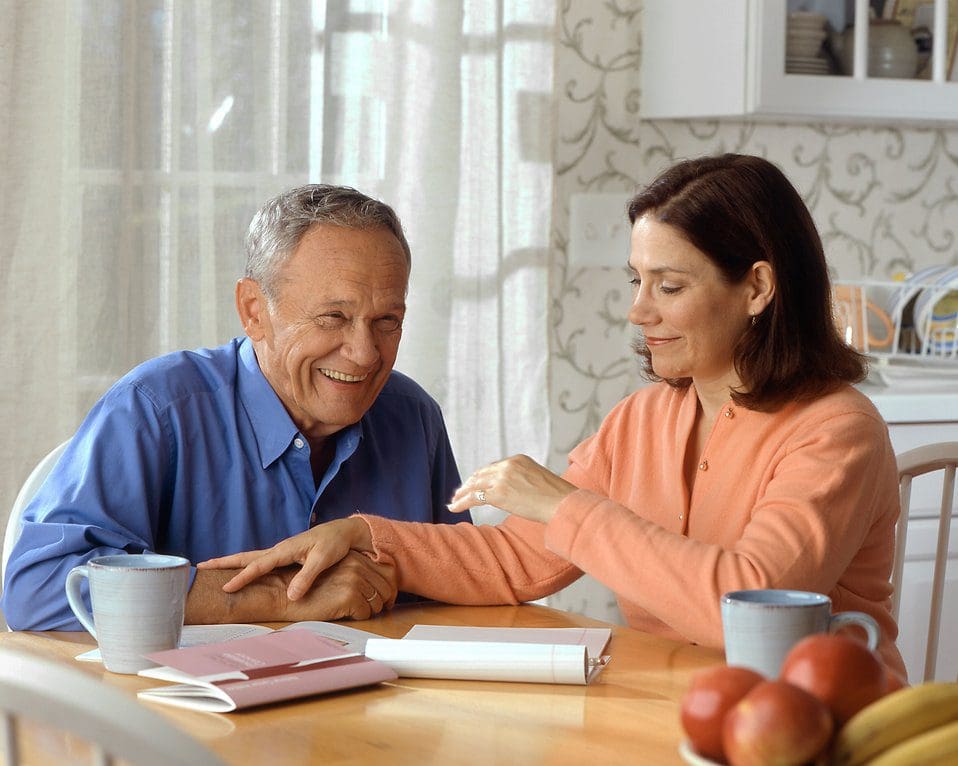 A careworker and a senior sit at a table laughing